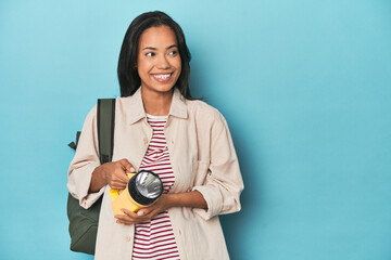 Filipina promoting excursions with lantern and backpack on blue studio
