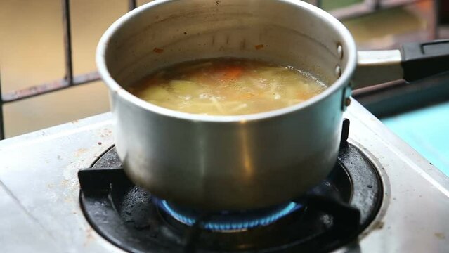 Chicken with noodles and potatoes cold soup in a small saucepan on the gas stove near the window lit the gas