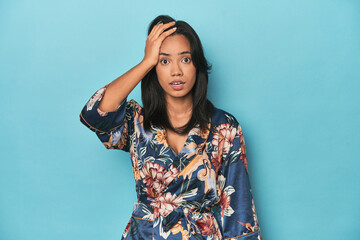 Filipina in floral kimono on blue studio being shocked, she has remembered important meeting.