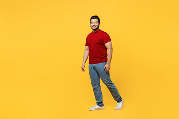 Fototapeta na wymiar Full body side profile view young cheerful fun happy Indian man he wearing red t-shirt casual clothes walking going looking camera isolated on plain yellow orange background studio. Lifestyle concept.