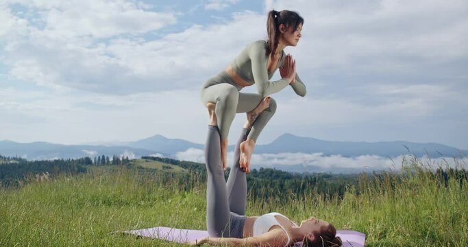 Couple of young sporty people in activewear stretching and practicing acro yoga together on fresh air. Concept of wellness, strength and balance. 