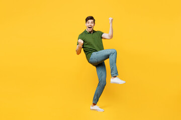 Full body side view young happy man he wears green t-shirt casual clothes doing winner gesture celebrate clenching fists say yes raise up hand isolated on plain yellow background. Lifestyle concept.
