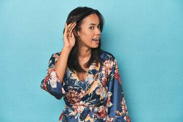 Filipina in floral kimono on blue studio trying to listening a gossip.