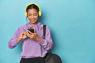 Filipina athlete with phone and headphones on blue studio background