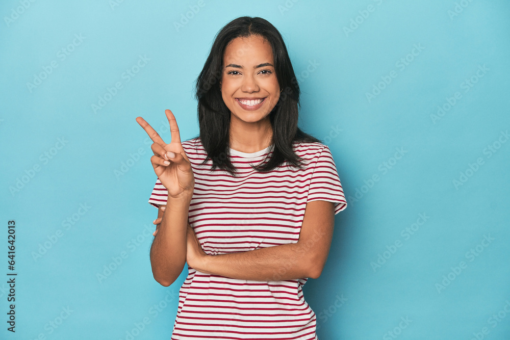 Wall mural filipina young woman on blue studio showing number two with fingers.