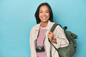 Filipina with camera and travel backpack on blue studio backdrop
