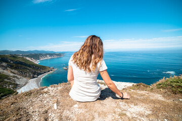 Serene paradise: Woman seated on rocky cliff's edge, savoring tranquil bliss in a beach haven.
