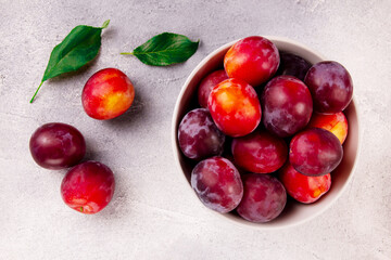 A bowl with ripe juicy plums on a gray background.