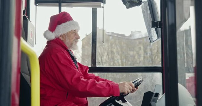 Side view of bus driver wearing Christmas hat sitting, dreaming. Old man with grey hair and beard holding hands on helm, looking forward, thinking. Concept of urban life.