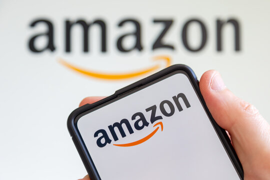 Hand holding a mobile phone with Amazon logo online marketplace ecommerce computer screen