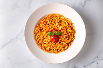 Tasty appetizing classic italian spaghetti pasta with tomato sauce, cheese parmesan and basil on plate and ingredients for cooking pasta on white marble table.