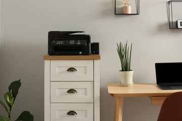Modern printer on chest of drawers near wooden table indoors