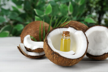 Bottle of organic coconut cooking oil, leaf and fresh fruits on white wooden table