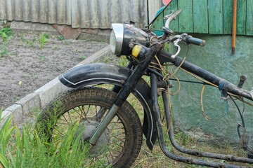 a frame from an old heavy rusty retro classic motorcycle in black with a front wheel fender a headlight and a fork stands in green grass on the street during the day