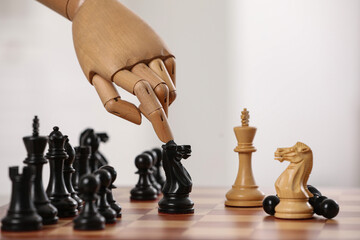 Robot moving chess piece on board against light background, closeup. Wooden hand representing...