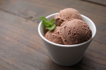 Bowl with tasty chocolate ice cream and mint leaves on wooden table. Space for text