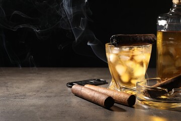 Cigars, ashtray, whiskey and cutter on grey table against black background. Space for text