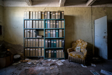 bookcase with binders and reading chair in an abandoned house