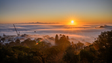 Auckland city above a sea of fog at sunrise. Sun starbursts shining through the clouds....