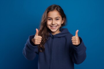 Lifestyle portrait photography of a happy kid female showing a thumb down against a royal blue background. With generative AI technology