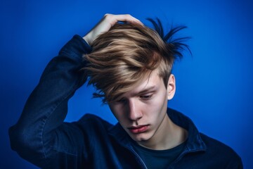 Close-up portrait photography of a beautiful boy in his 20s scratching head in gesture of confusion against a royal blue background. With generative AI technology