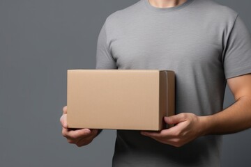 Mockup: Cropped view of a man holding a cardboard box against a grey background, ready for presentation.