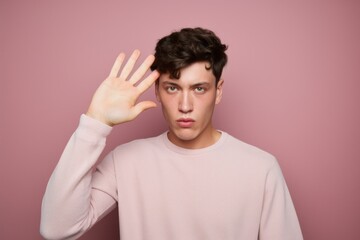 Medium shot portrait photography of a beautiful boy in his 20s doing loser gesture mocking against a dusty rose background. With generative AI technology