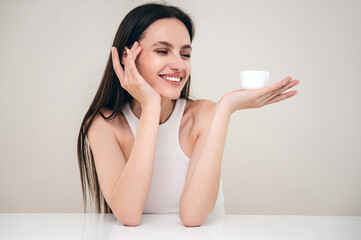 Smiling woman applying moisturizing cream under eyes