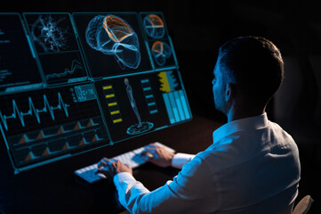 A caucasian man sits in the dark in front of a virtual menu and types on a keyboard. human brain research.