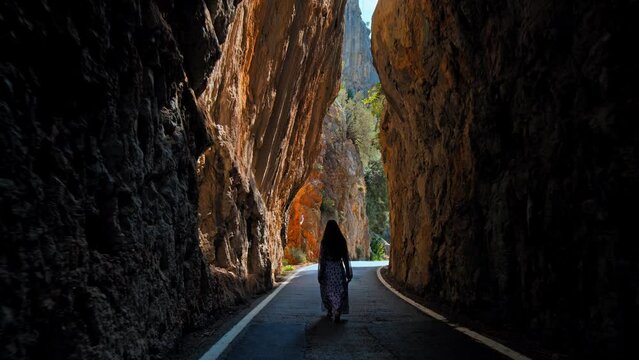 Beautiful Girl in a dress walking in slow motion into a rocky mountain tunnel. An adventurous woman enjoying wildlife in Mallorca, Spain.