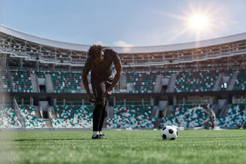 Professional male football, soccer player on stadium background. African fit athlete practicing, playing excited