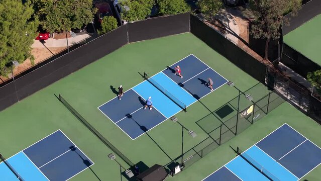 Aerial view circling, looking down over young adult foursome playing pickleball on blue sunny tennis court