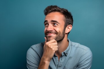 Close-up portrait photography of a joyful boy in his 30s putting the hand on the chin as if thinking against a soft blue background. With generative AI technology