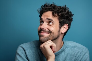 Fototapeta premium Close-up portrait photography of a joyful boy in his 30s putting the hand on the chin as if thinking against a soft blue background. With generative AI technology
