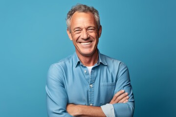 Obraz premium Medium shot portrait photography of a happy mature man crossing the arms against a soft blue background. With generative AI technology
