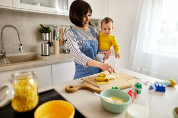 Mother feeding her baby boy with banana in the kitchen