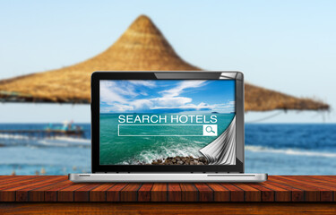 Search hotels website on laptop computer screen, a straw beach umbrella and tropical beach on...