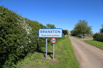 A reflective blue and white sign at the entrance to Branxton village in Northumberland, England, UK. © Wendy