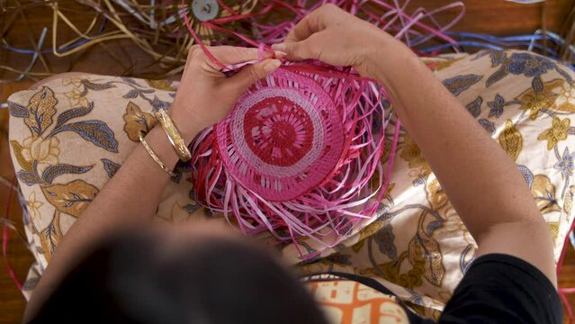 Overhead View Of An Indigenous Woman Hand Weaving A Colorful Basket.