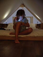 Naklejka premium Concentrated boy reading book with flashlight