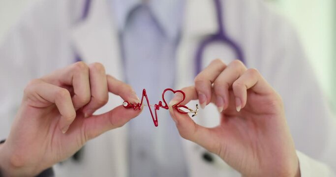 Practitioner doctor holding small red pin as badge of heart rate. Specialist cardiologist represents heart sphere. Doctor in hospital robe at private clinic