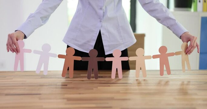 Female with paper ornament figures cut as garland on string above wooden table. Concept of team building and teamwork in corporate office slow motion