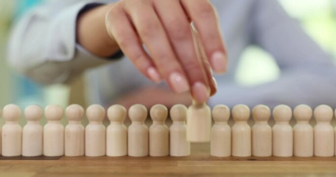 Woman with group of small wooden human figures on desk in office. Lady moves pawn ahead. Concept of failure to maintain group work and people condemnation slow motion