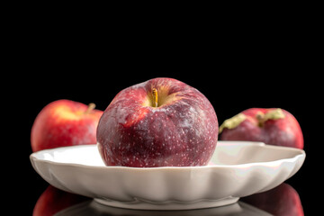 Three juicy dark red apples on a white ceramic plate, macro, isolated on black background.