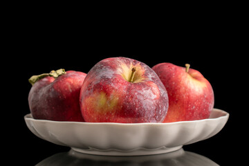 Three juicy dark red apples on a white ceramic plate, macro, isolated on black background.