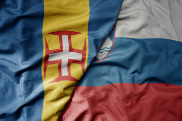 big waving national colorful flag of madeira and national flag of slovenia .