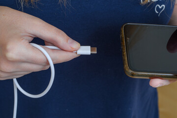 Kobieta podłączająca kabel od ładowarki USB typu c do telefonu - obrazy, fototapety, plakaty