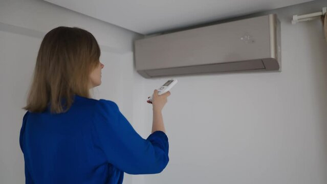 Woman holding remote control aimed at the air conditioner.