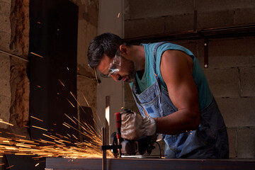 Focused male artisan cutting metal with disk grinder