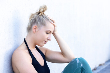 In a candid portrayal of strength through adversity, a Caucasian blonde millennial sportswoman, donning her sports outfit, grapples with a sport injury. With a hand on her head, she experiences a